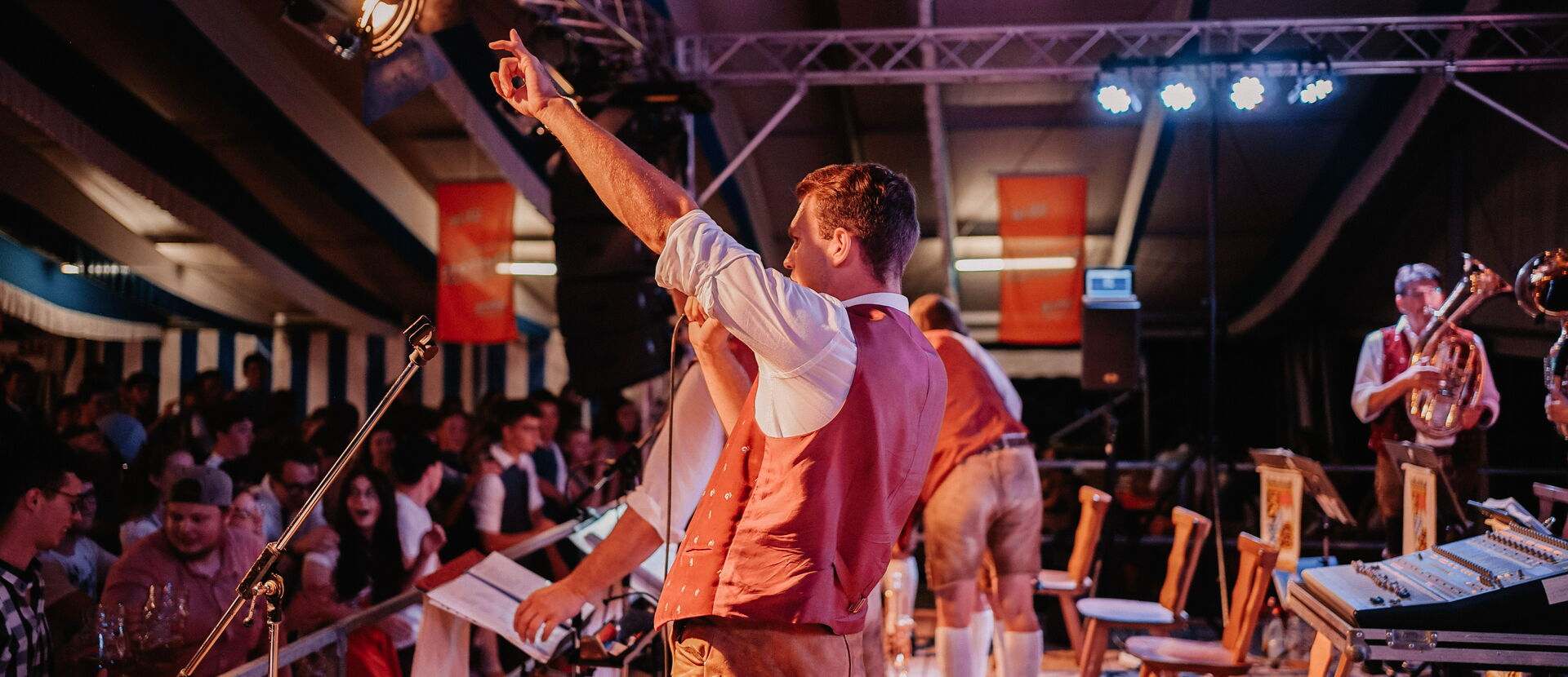 Bayernkapelle Toni Schmid Die Musiker auf einer Bühne in einem Bierzelt vor feierndem Publikum